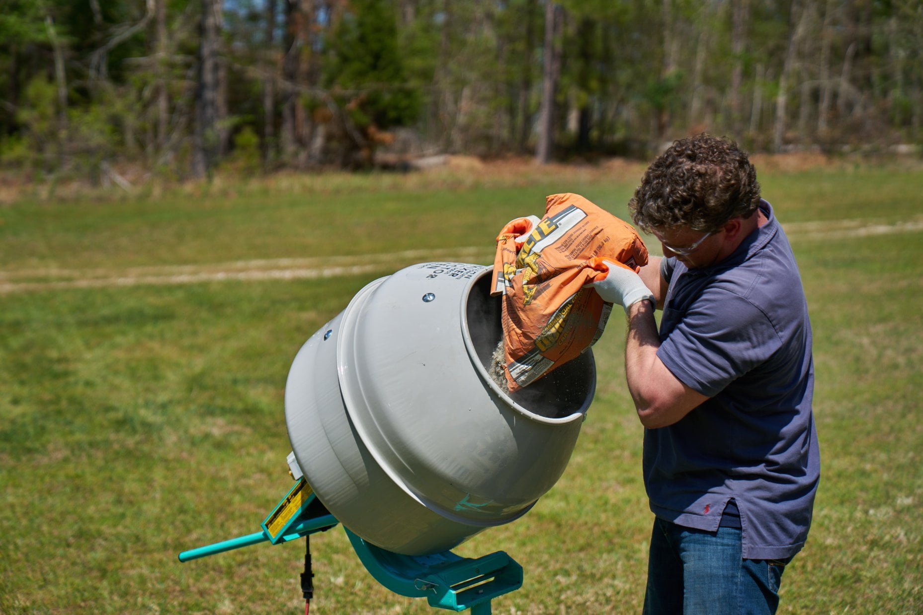 man pouring quikrete concrete mix into drum