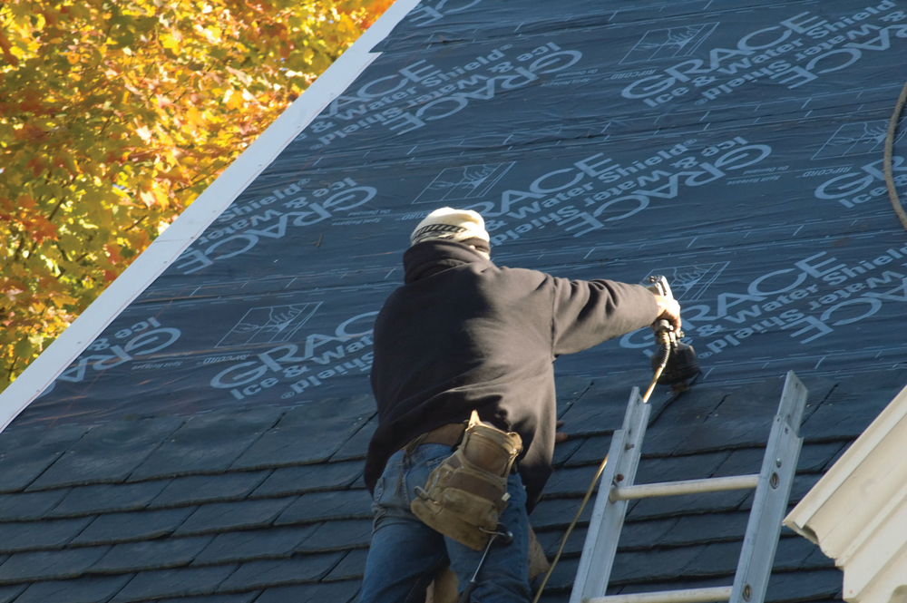 worker applies grace ice water shield with staple gun to roof