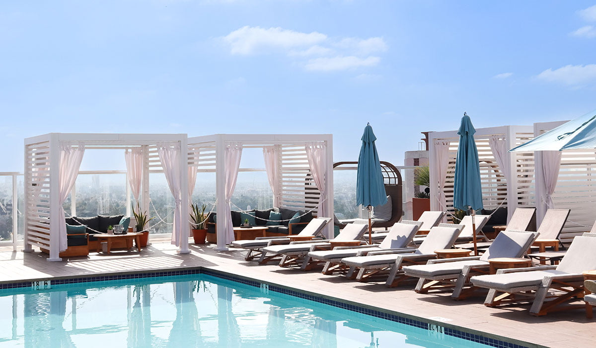 White StruXure CabanaX poolside with lounge chairs and blue umbrellas